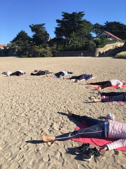 Groupe de yoga allongés en cercle sur une plage entrain de pratiquer une séance de relaxation