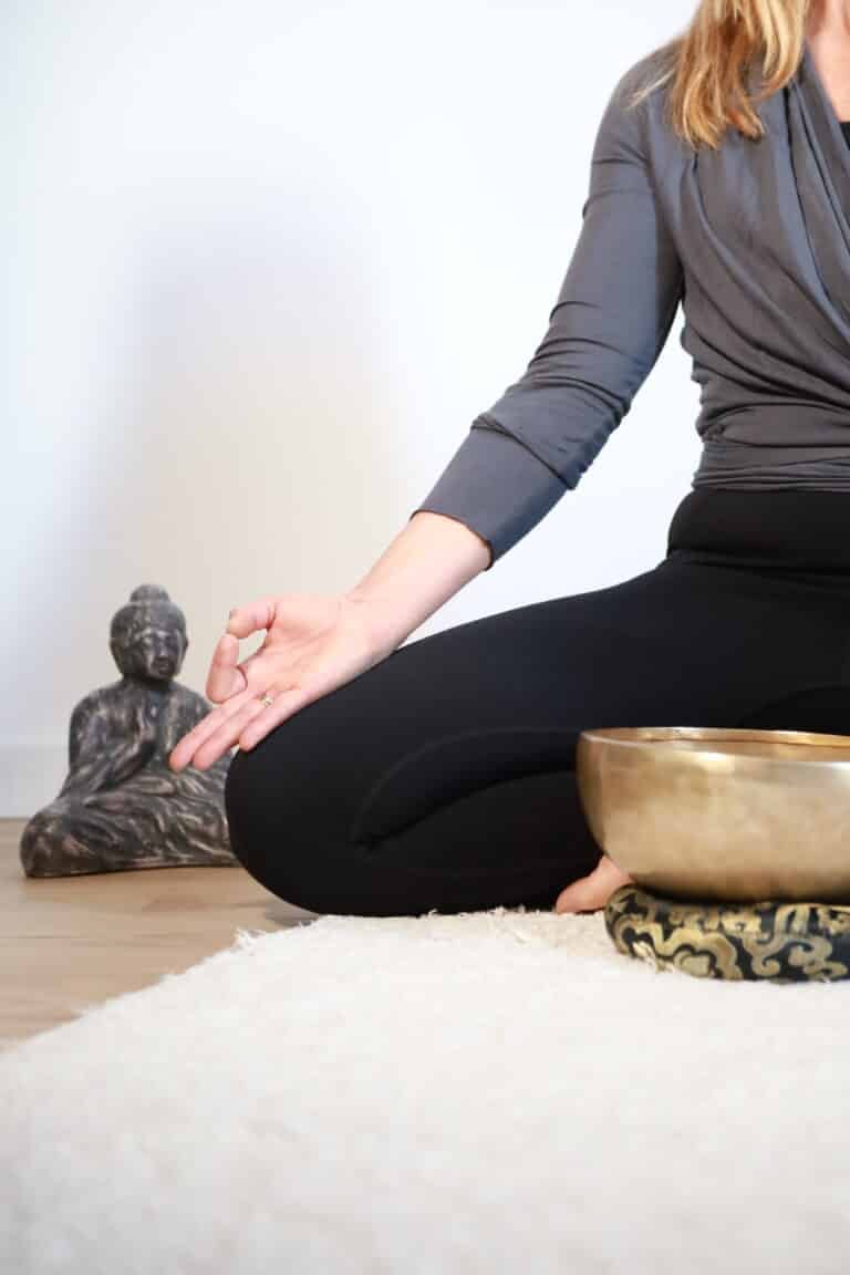 image tronquée de gwladys en séance de méditation sur un tapis avec petit buddha et bol tibétain