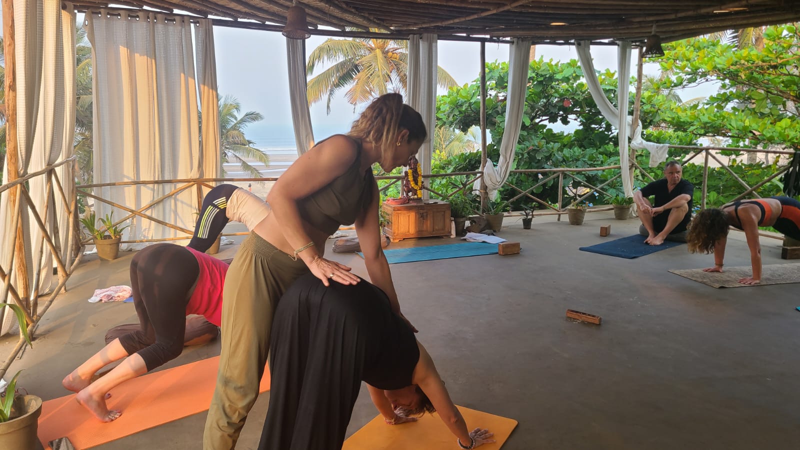 Gwladys corrige la posture d'une élève pendant un cours de yoga dans un shala avec vue mer et arbres tropicaux dan sle centre Nalanda Retreat Wellness and Spa Resort à Mandrem, Goa, Inde.