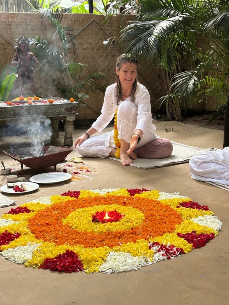 Photo de Gwladys en habit traditionnel de yogi assise devant un parterre de composition florale durant une cérémonie de bienvenue puja