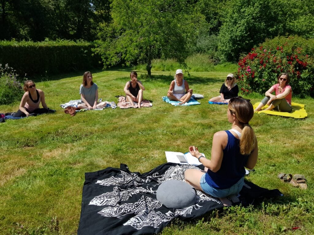 Photo représentant Gwladys assise dans un jardin verdoyant face à ses yogis, donnant un cours de yoga en extérieur