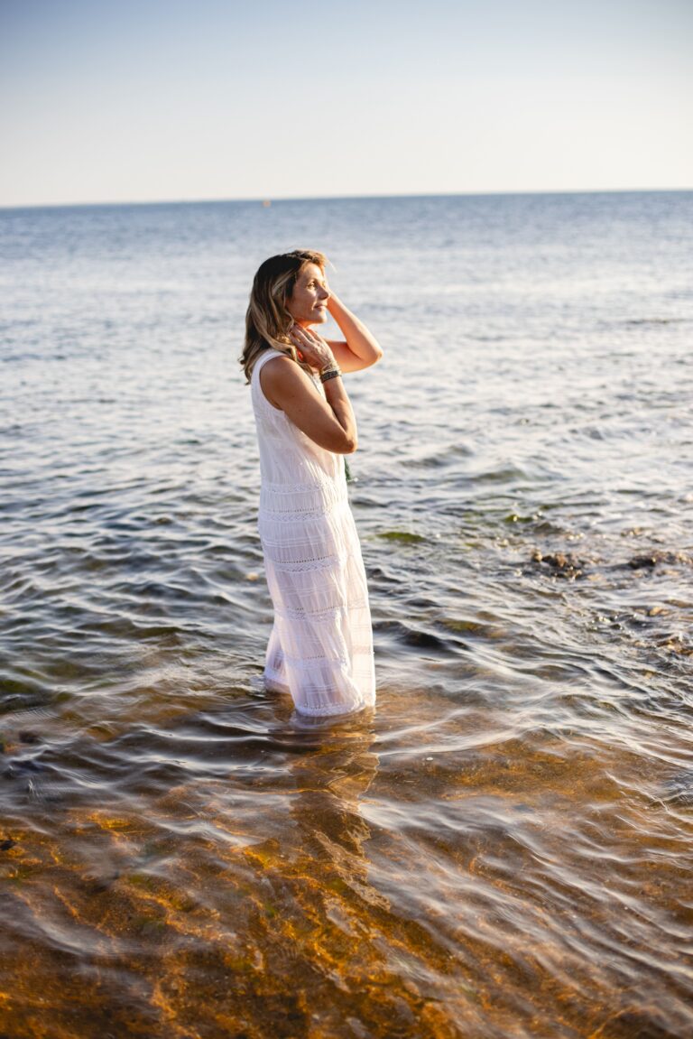 Photo de Gwladys débout, vêtue d'une robe blanche, les pieds dans la mer